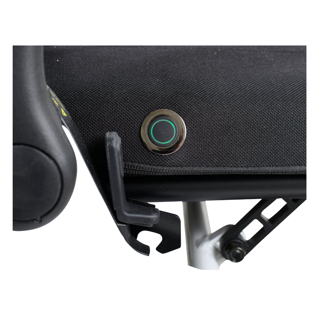 Close-up of a black fabric seat with a circular metal button featuring a green LED light, part of Golden Tech Accessories For The Ally Powerchair. Below the seat, find a black plastic hook and phone holder on a white metal frame.